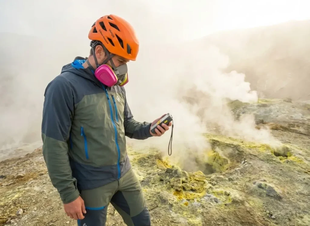 Hiker wearing a 3M respirator and Black Diamond helmet inspecting a sulfur vent on an active volcano.