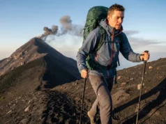 Volcano Hiking Tours: A Hiker’s Technical Skill Guide Hiker ascending Acatenango volcano wearing a Patagonia jacket and Osprey backpack with Fuego erupting in the background.