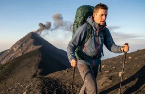 Volcano Hiking Tours: A Hiker’s Technical Skill Guide Hiker ascending Acatenango volcano wearing a Patagonia jacket and Osprey backpack with Fuego erupting in the background.