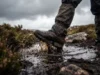 Best Waterproof Hiking Socks Tested: Sweat vs. Rain Close up of hiking boots stepping deep into a muddy, water-filled bog, splashing dirty water.