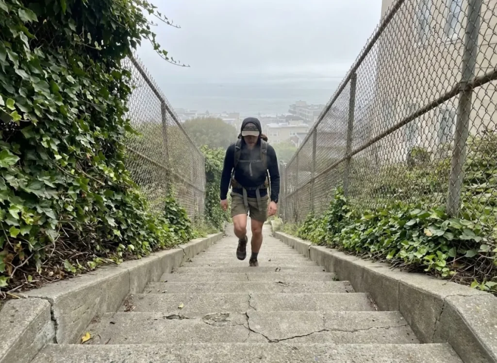 A hiker climbing steep, ivy-lined concrete stairs with a foggy view in the background.