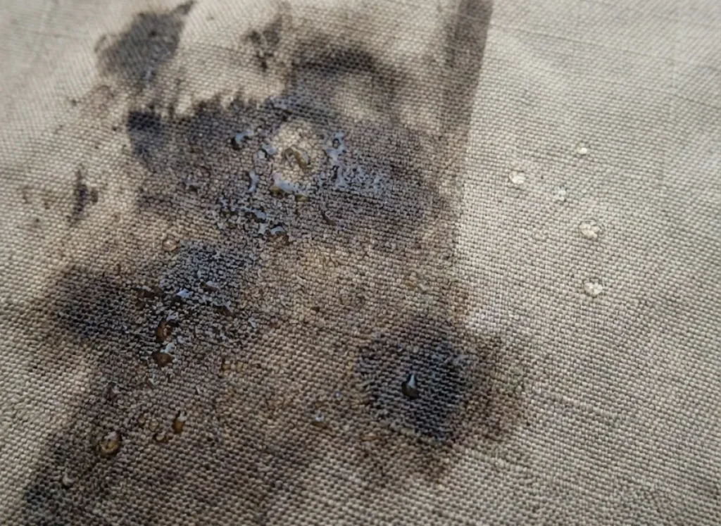 Close-up macro shot of dirty waterproof fabric absorbing water droplets instead of repelling them due to contamination.