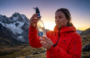 The 0.1 Micron Myth: Filter Pore Size & Virus Protection Professional hiker in a red Arc'teryx jacket inspecting a Sawyer Squeeze water filter against a mountain backdrop during golden hour.