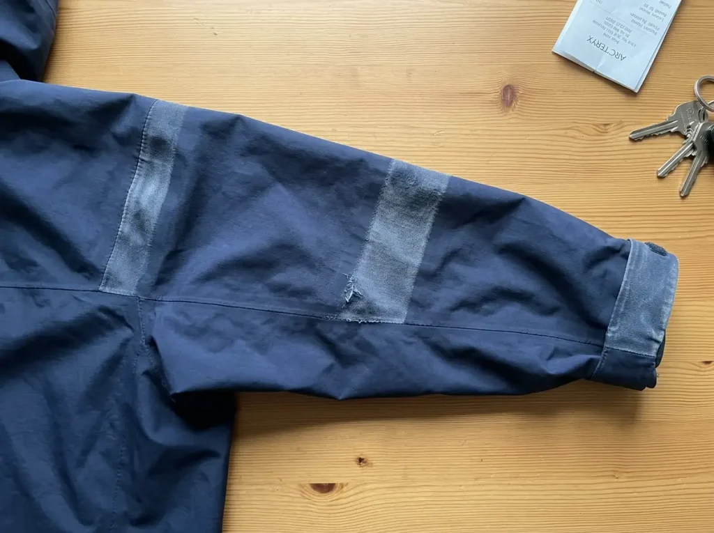Worn rain jacket shoulder showing abraded fabric where pack straps ride