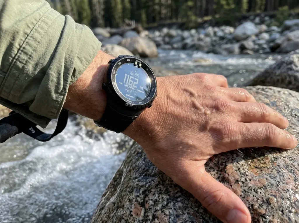 Suunto Core ABC watch on a wrist beside a stream crossing on a hiking trail
