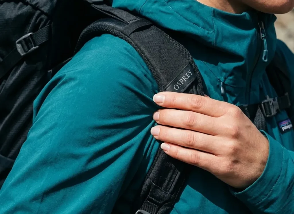Close-up of a hiker tightening a heavy backpack load lifter, showing the intense compression of the shoulder strap against a waterproof jacket.