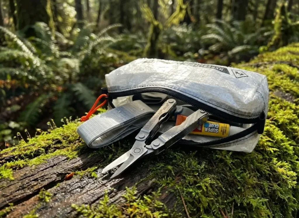 A Hyperlite Mountain Gear Dyneema pouch resting on moss, revealing a Leatherman Micra and repair patches, lit by dappled forest sunlight.
