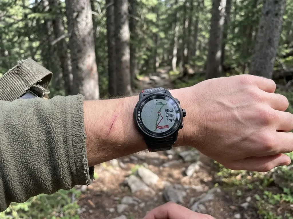 Coros Apex 2 Pro GPS watch on a wrist under dense conifer canopy on a shaded trail