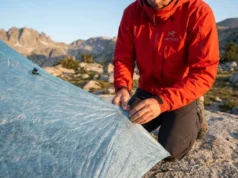 The Modular Hiking Gear Repair Kits Guide: DIY & Ultralight A professional hiker in an Arc'teryx jacket performing a field repair on a Zpacks Dyneema tent in a high-alpine granite landscape during golden hour.