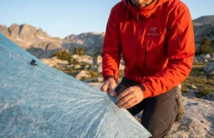 The Modular Hiking Gear Repair Kits Guide: DIY & Ultralight A professional hiker in an Arc'teryx jacket performing a field repair on a Zpacks Dyneema tent in a high-alpine granite landscape during golden hour.