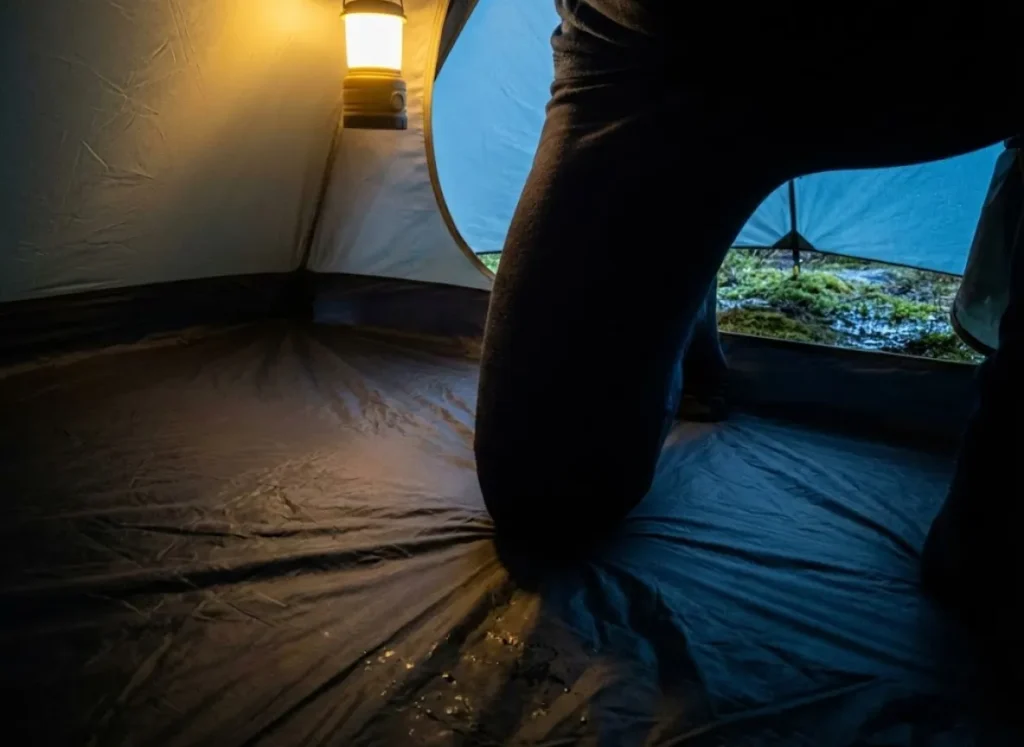 Interior shot of a camper kneeling on a tent floor, illustrating the high pressure exerted by knees that requires high hydrostatic head ratings.
