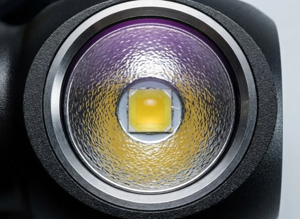 Extreme macro close-up of a headlamp LED emitter and orange-peel reflector, showing the yellow phosphor chip and anodized aluminum texture.
