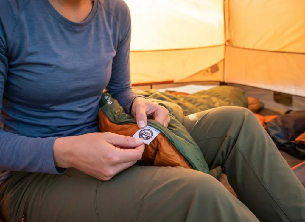 A hiker inside a tent inspecting the certification tags on a down sleeping bag.