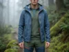 Survival Physics: Thermal Conductivity of Wet Cotton & Wool A professional hiker wearing Arc'teryx and Smartwool layers in a misty, cold rainforest, showcasing the texture of merino wool and water-resistant technical fabrics.