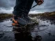 Waterproof Hiking Socks: The Realist’s Buying Guide Close-up of muddy hiking boots submerged in a cold stream, demonstrating the need for waterproof socks.