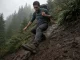 4 Lug Depth Mistakes That Wreck Muddy Descents Hiker in low-cut hiking shoes braking heel-first down a muddy slope, deep lug tread biting the grade