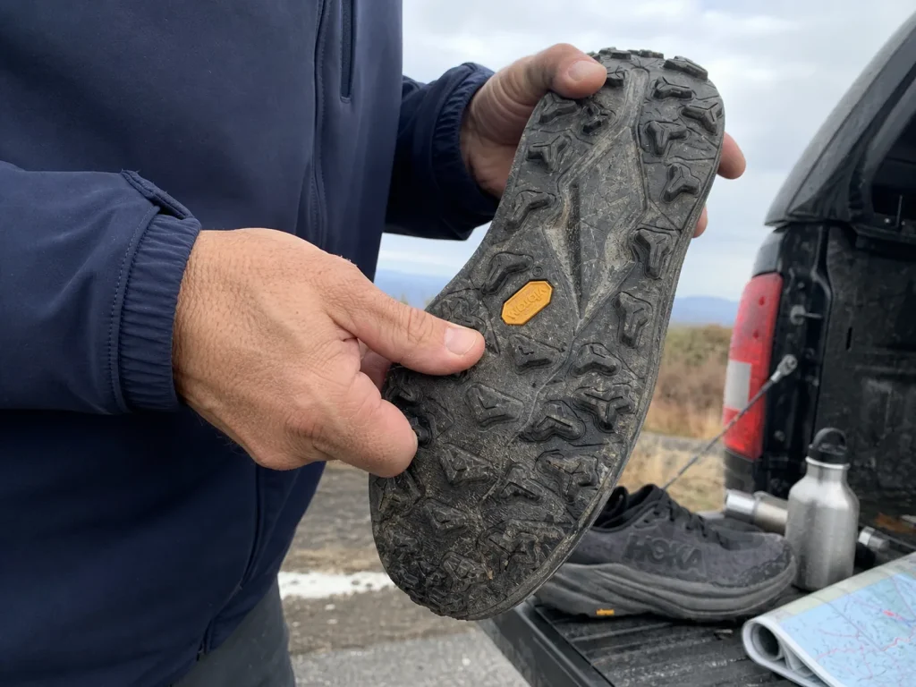 Close-up of a deep-lug hiking shoe outsole held up to compare lug depth in millimeters