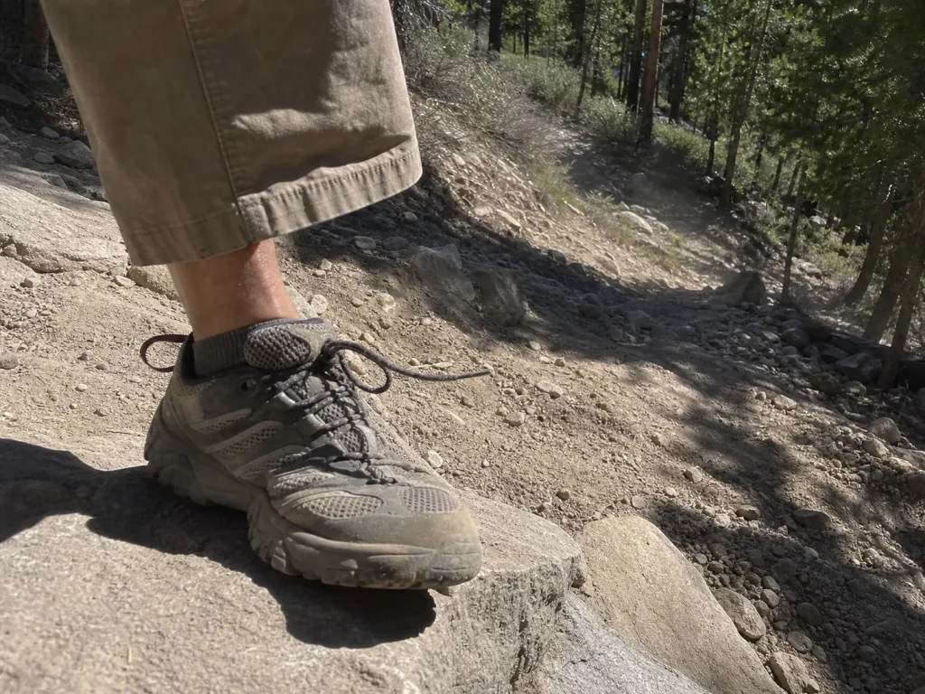 Worn hiking shoe toe bumper pressed against a rock step on a steep descent