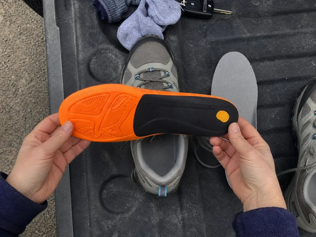 Hands holding a Superfeet Hike Support insole over a hiking shoe at a trailhead tailgate