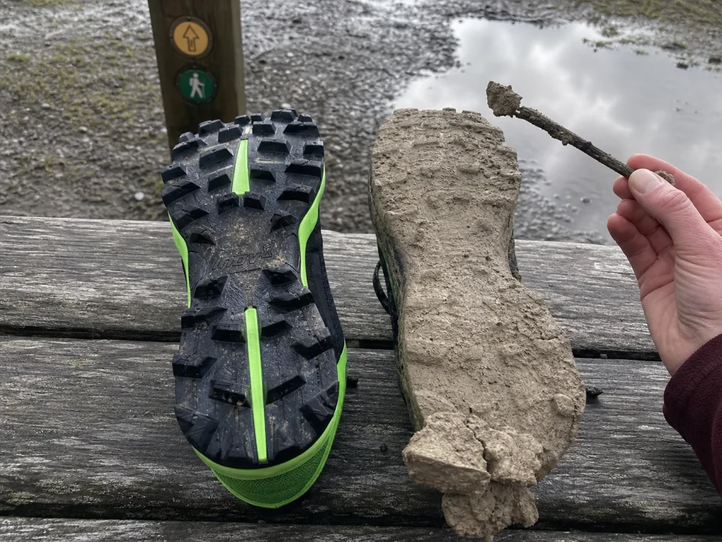 Two hiking shoe outsoles side by side, one with tread channels packed solid with clay and one shedding clean