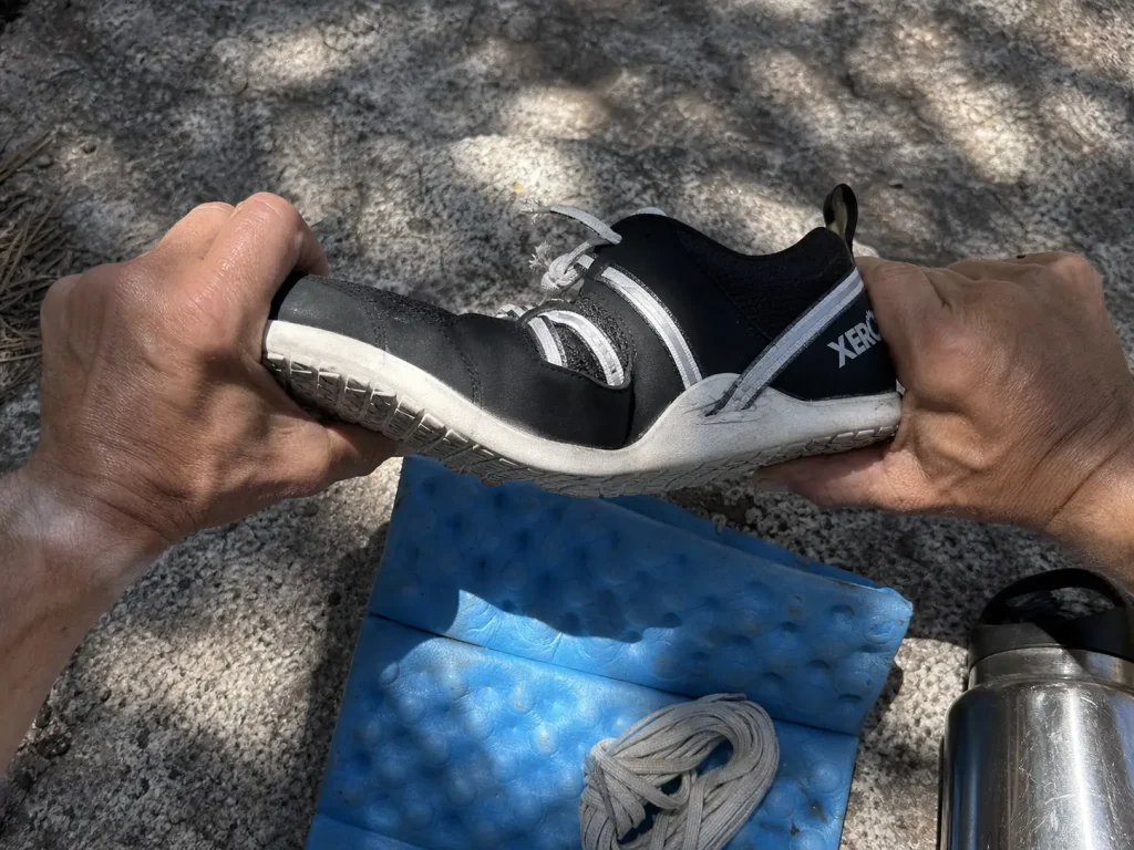 Hands twisting a low-cut hiking shoe to test midsole stiffness before buying it for wet crossings