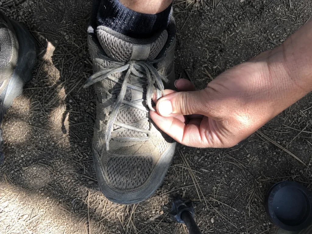 Hands tying a surgeon's knot to lock the heel on a low-cut hiking shoe