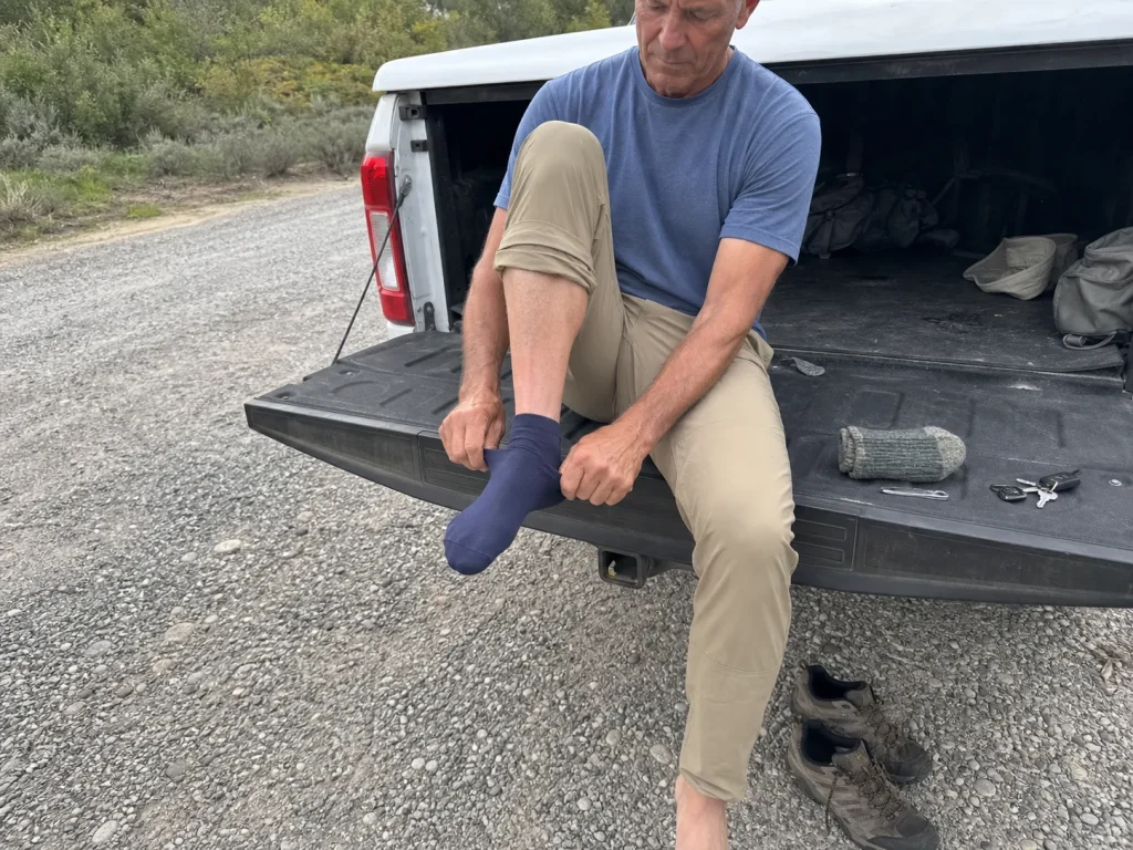 Hiker pulling on a Fox River liner sock at a trailhead tailgate before the outer sock