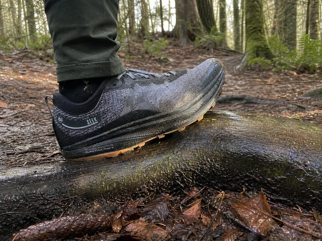 Hiker sitting on a log pouring water out of a waterproof hiking shoe after a muddy crossing
