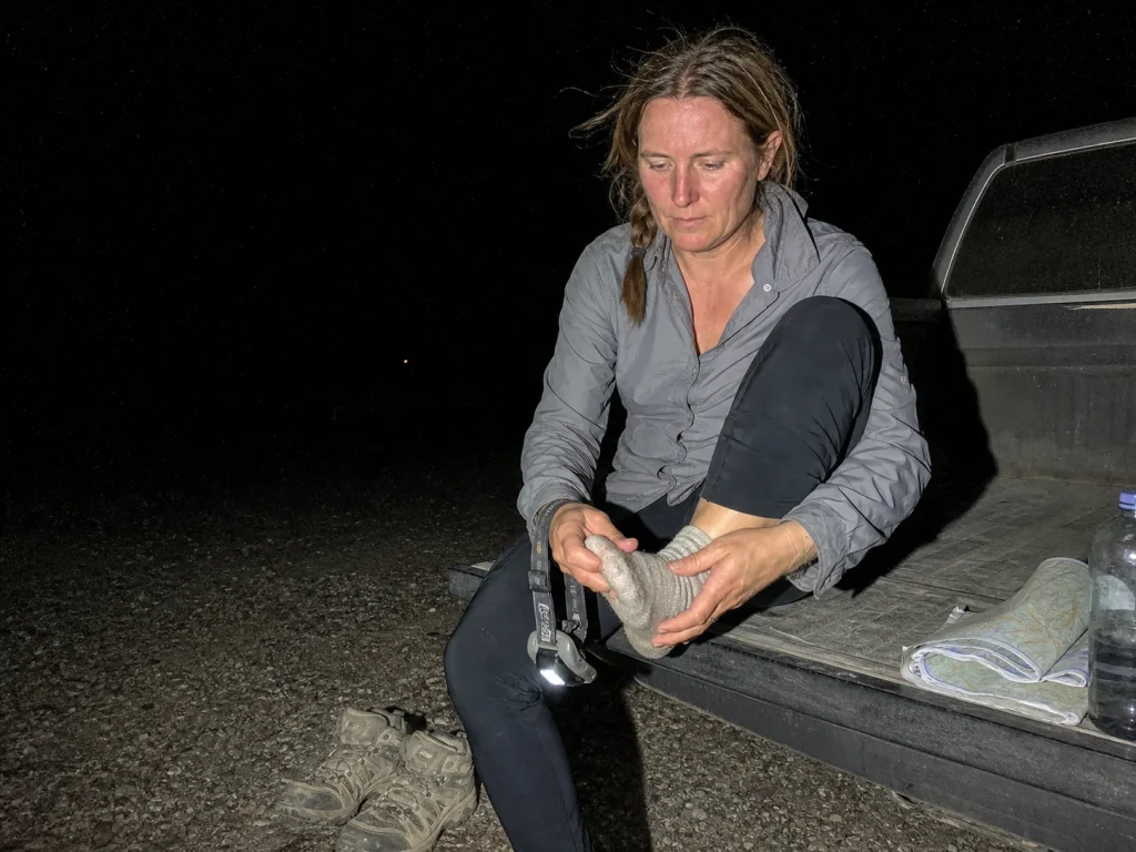 Hiker checking her foot through a sock at the tailgate after a long descent at dusk