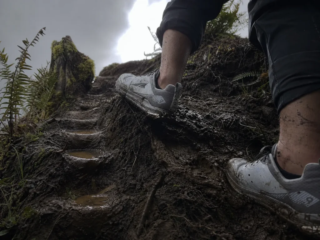 Hiker plunge stepping heel first down a muddy slope, directional lugs biting against the grade
