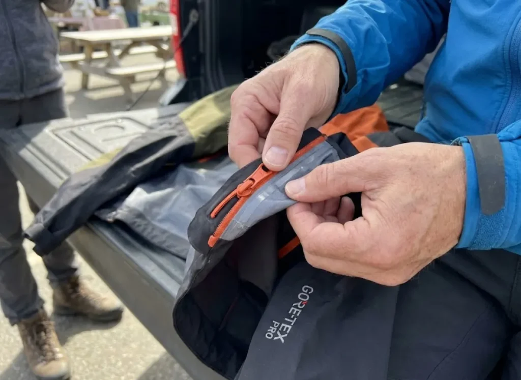 Hands inspecting Arc'teryx jacket zipper and seam tape for authentication markers