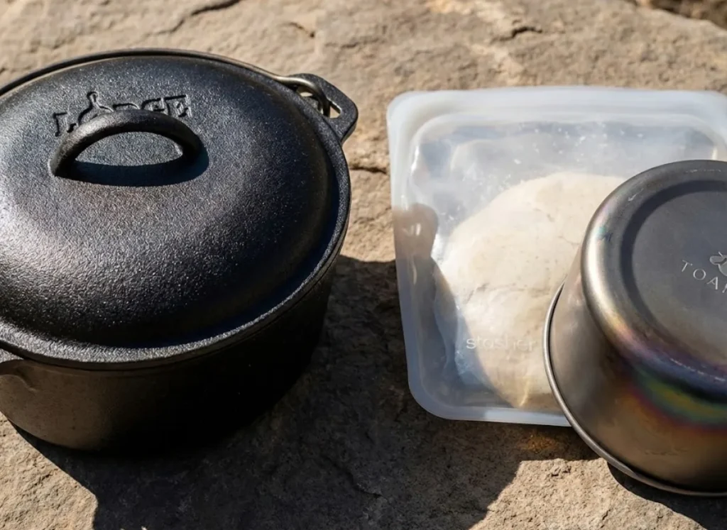 Side-by-side gear comparison showing a heavy Lodge cast iron pot versus an ultralight Stasher silicone bag and Toaks titanium pot on a rock.