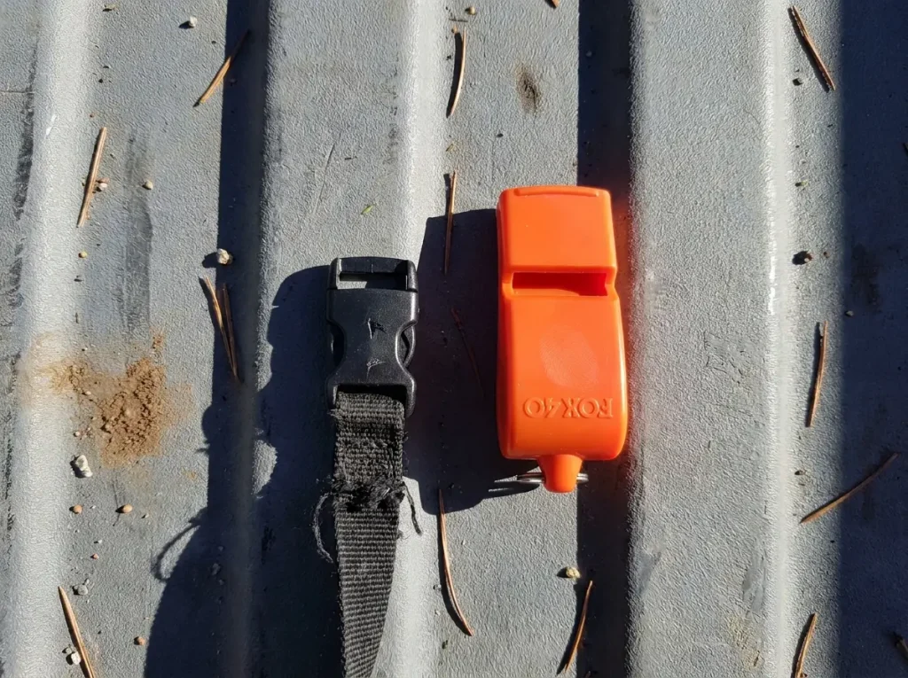 A small backpack buckle whistle beside a larger dedicated Fox 40 emergency whistle showing the size difference