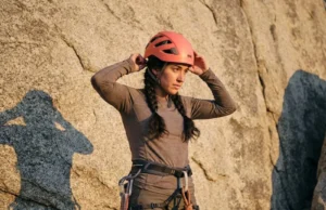 How to Choose a Climbing Helmet That Actually Fits Female climber adjusting Petzl Borea helmet fit at base of granite wall with braided hair