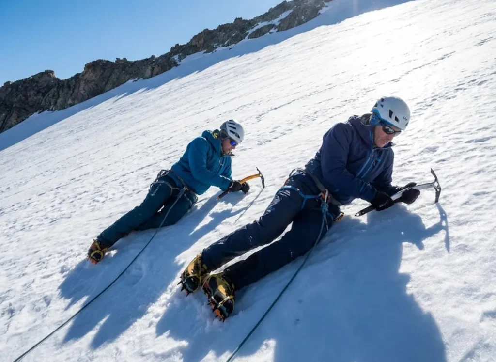 Professional mountain mentor teaching ice axe self-arrest technique on alpine snow slope
