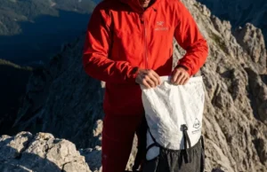 Distribute Pack Weight to Center of Gravity A professional hiker on a rocky ridge wearing an Arc'teryx jacket and Hyperlite Mountain Gear backpack, demonstrating perfect posture and balance against a dramatic alpine sky.