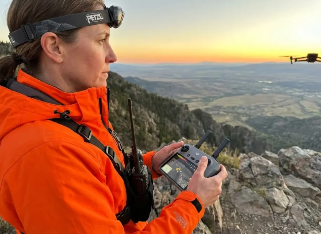 SAR volunteer operating drone in high visibility orange gear during search and rescue operation