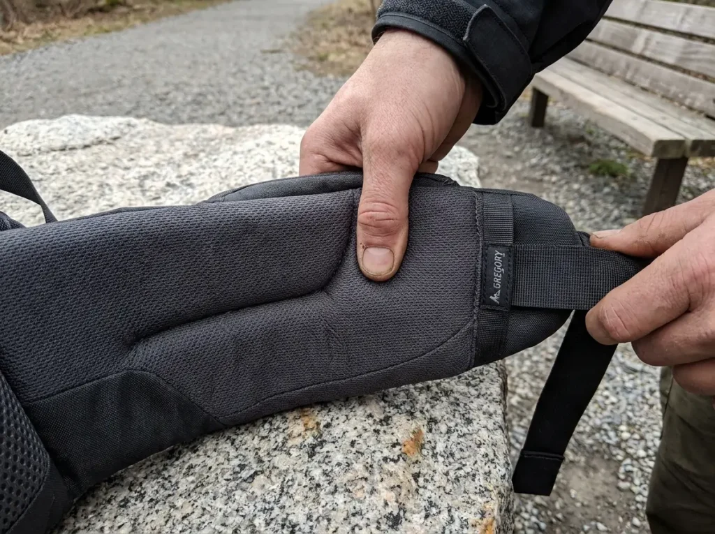 Close-up of a padded backpacking hip belt wing showing the dual-density foam behind moldable hip belt fit