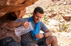 Heat Stroke vs Heat Exhaustion: What Hikers Need to Know Hiker cooling down with hydration bladder and cooling towel on desert canyon trail in extreme heat