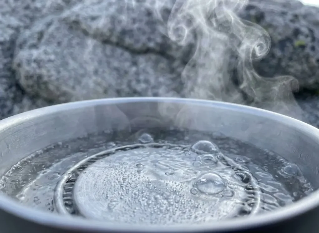 Macro photography of water boiling in a Jetboil stove at high altitude, highlighting bubble formation and steam physics against a blurred granite background.