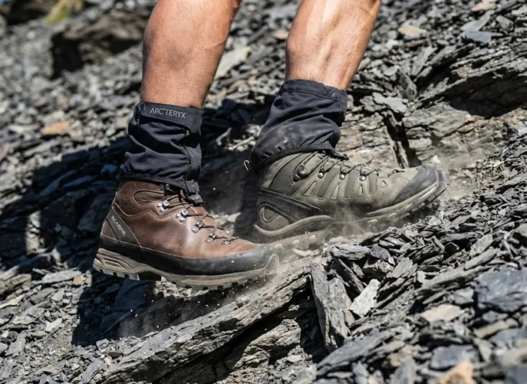 Action close-up of Scarpa and Salomon hiking boots digging into sharp scree, demonstrating abrasion resistance and material tension under heavy load.