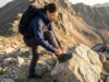 Downhill Heel Slippage? The Lacing Fix That Actually Works Hiker adjusting hiking boot laces on steep mountain descent to prevent heel slippage