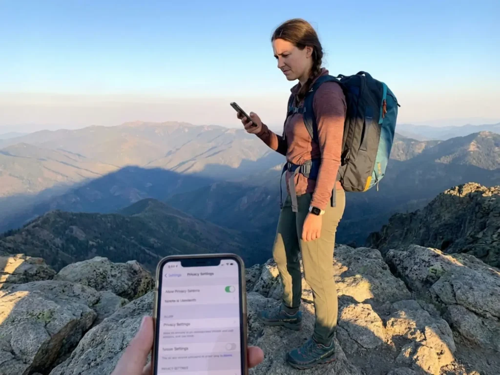 Woman hiker reviewing phone privacy settings on mountain summit before posting