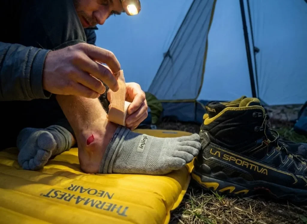 Hiker treating heel blister at camp caused by improper lacing and heel slippage