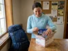 Mail Drops vs Buying Food on Trail (What Actually Works) Thru-hiker opening USPS resupply box at trail town post office with dehydrated meals and backpacking food