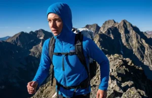 Manage Sweat with Grid Fleece Capillary Action A professional hiker on an alpine ridge wearing a textured blue grid fleece, backlit by the sun to highlight the fabric's engineering.
