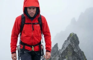 Open Pit Zips to Regulate Core Temp While Moving A professional mountaineer hiking in a misty alpine environment wearing a red Arc'teryx hard shell jacket, showcasing high-end outdoor gear photography.