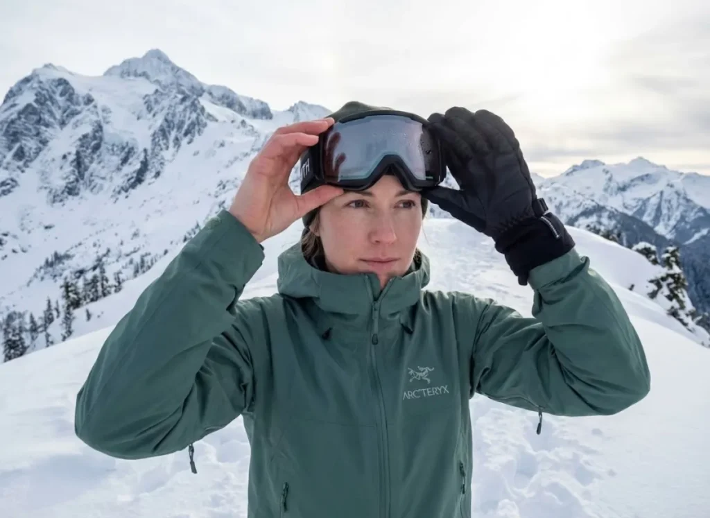 Winter hiker examining fogged Smith goggles on snowy alpine ridge above treeline