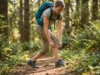 Why Roll Up Hiking Pants Beat Shorts (Most Summer Days) Female hiker adjusting roll-up hiking pants on summer forest trail with sunlit vegetation