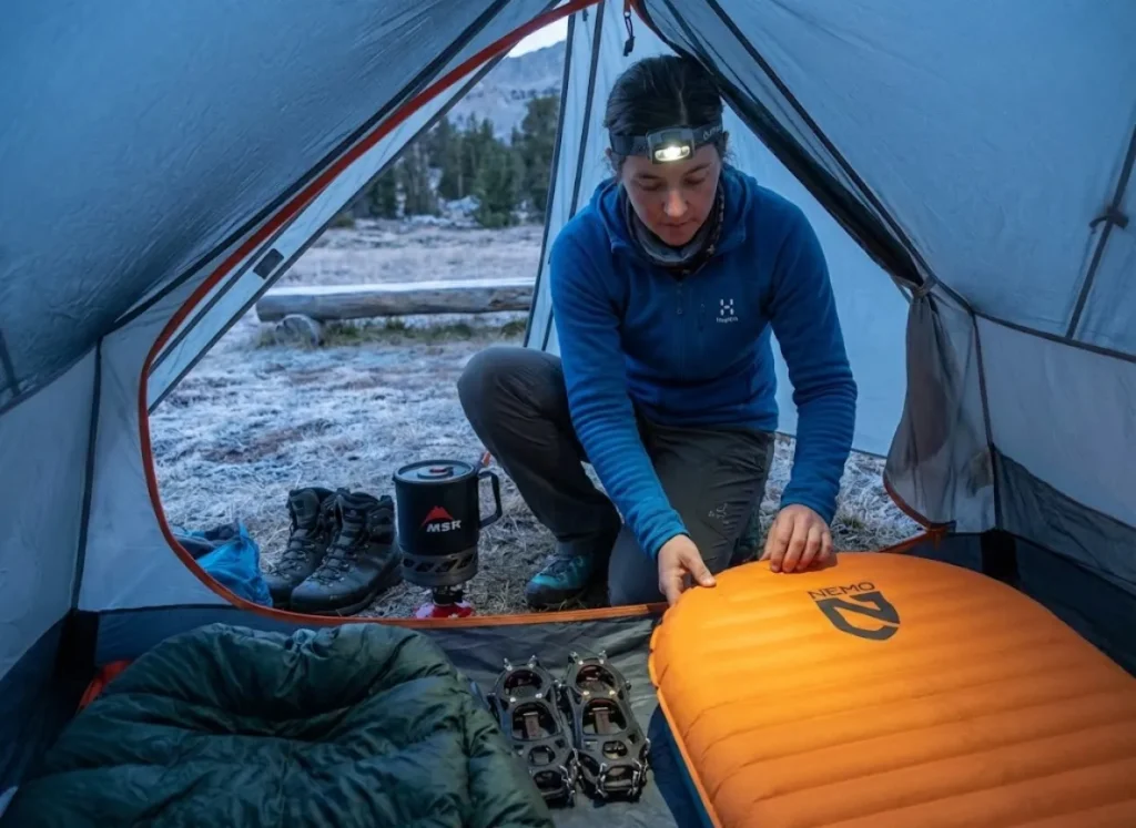 Hiker organizing high R-value cold weather gear in tent during shoulder season camping
